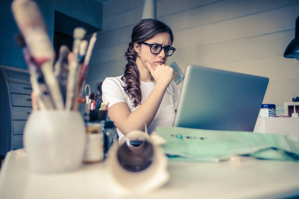 A woman sitting working at her laptop with a confused look.